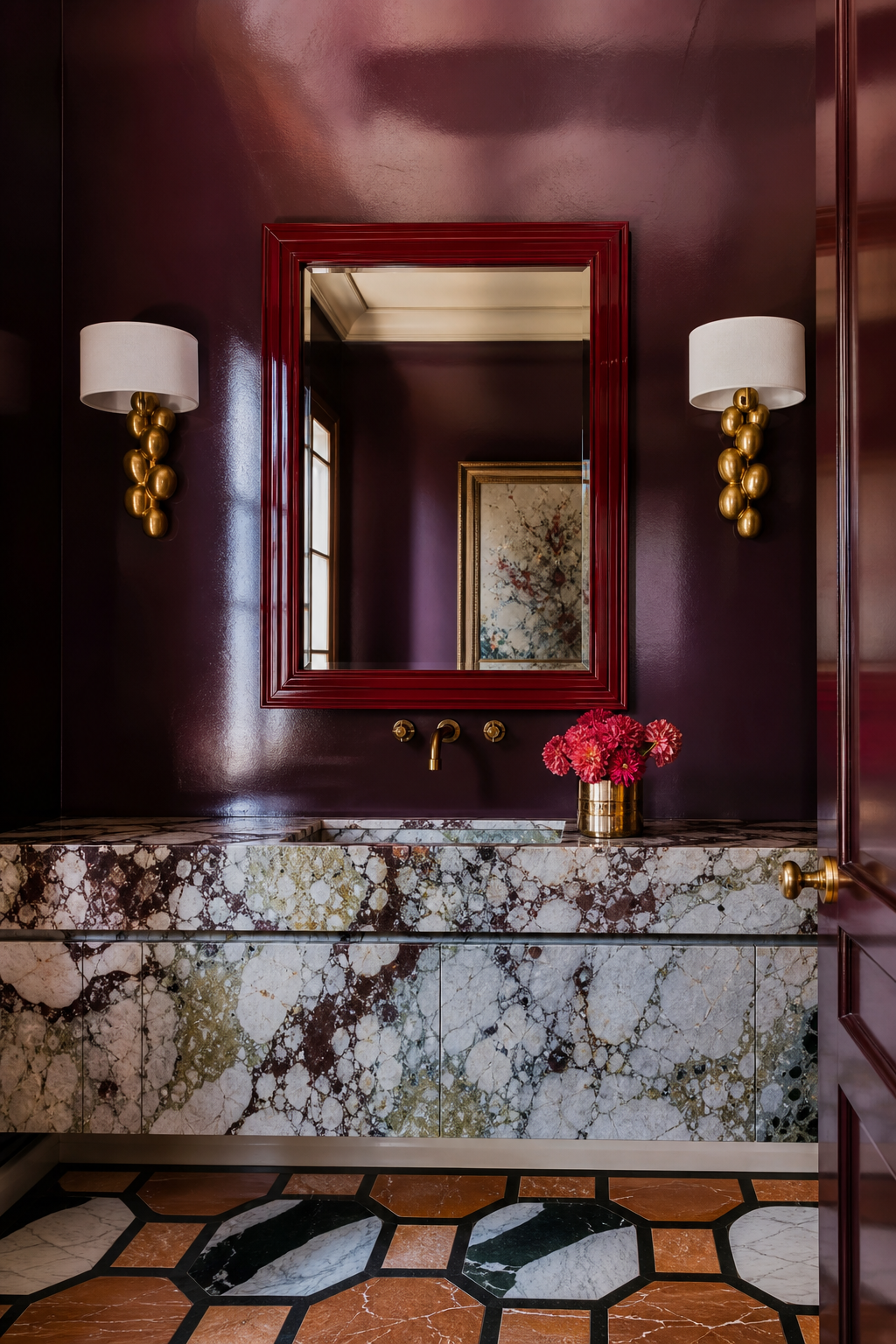 Bold powder room with lacquered plum walls, colorful marble vanity, brass sconces, and red mirror