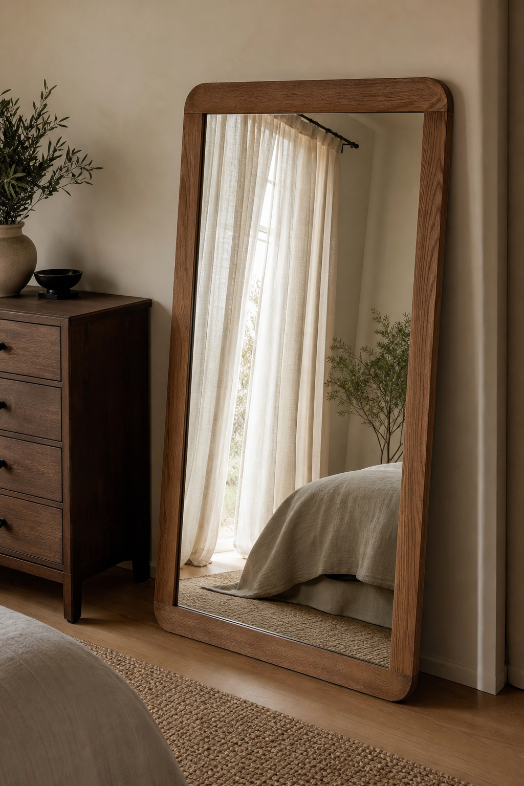 Bedroom mirror reflecting soft window light and linen curtains