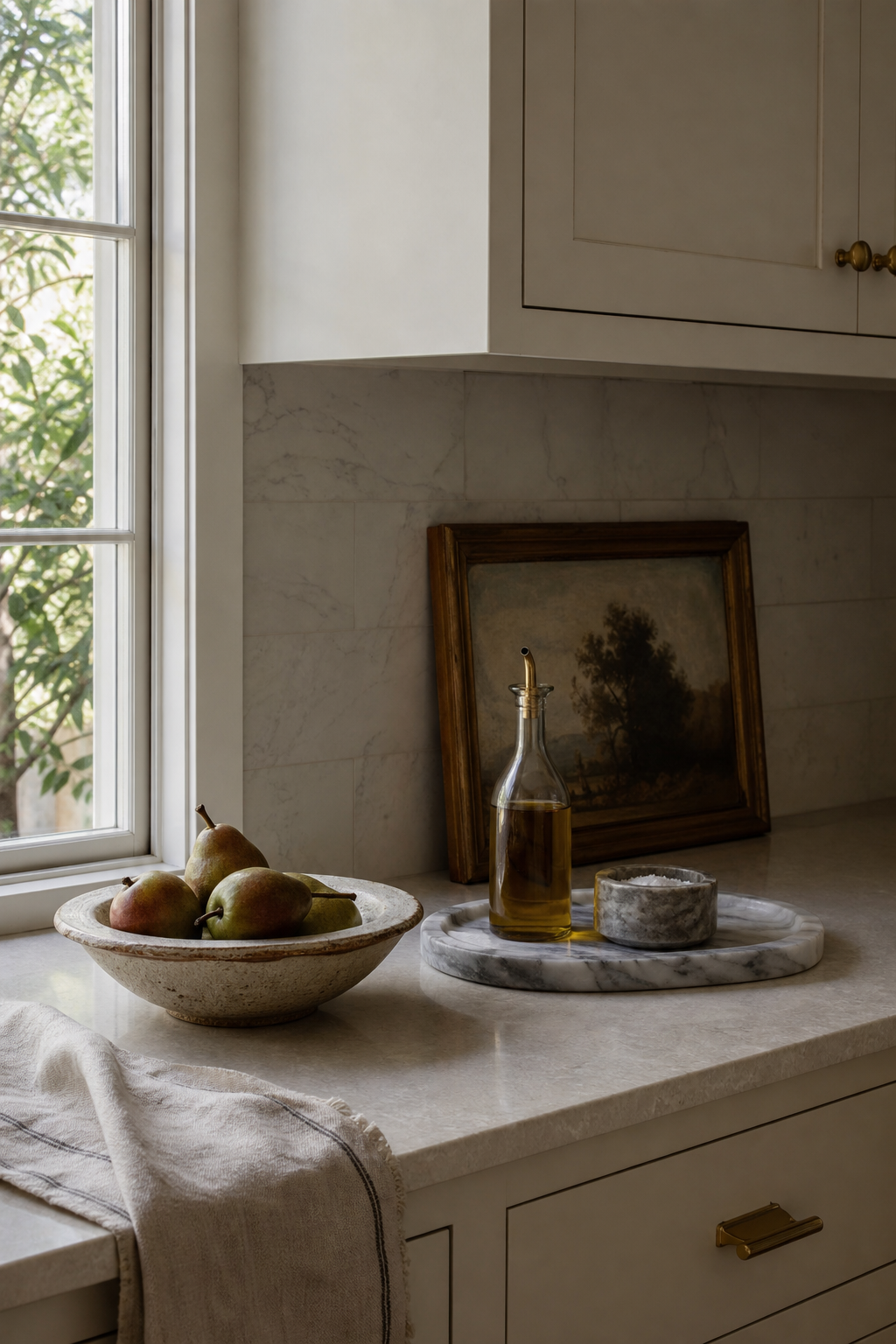 Very small kitchen counter styled with marble tray, ceramic bowl, linen towel, and framed art